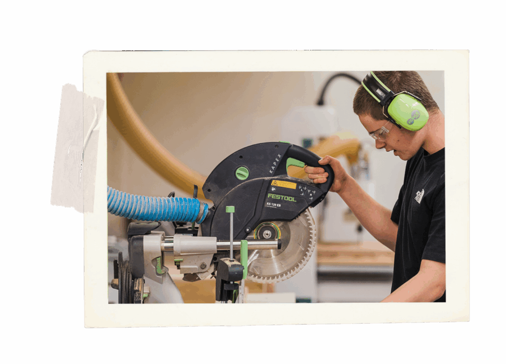 Young student using a drop saw, appears to be using the correct safety equipment.