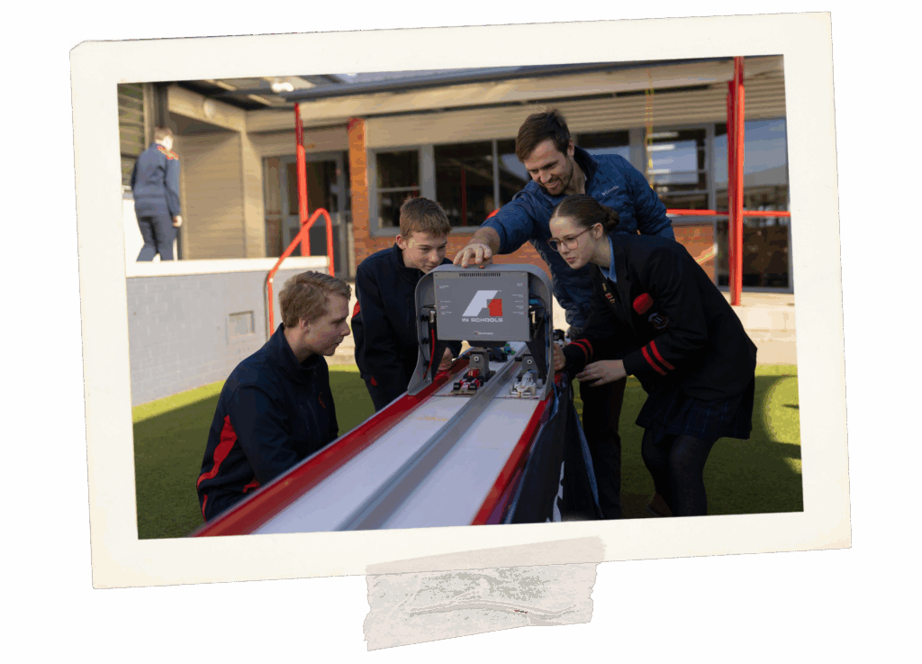 Students and a teacher playing with a F1 slot car. Looks like an fancy slot car machine. The slot car machine only allows for 2 car slots.