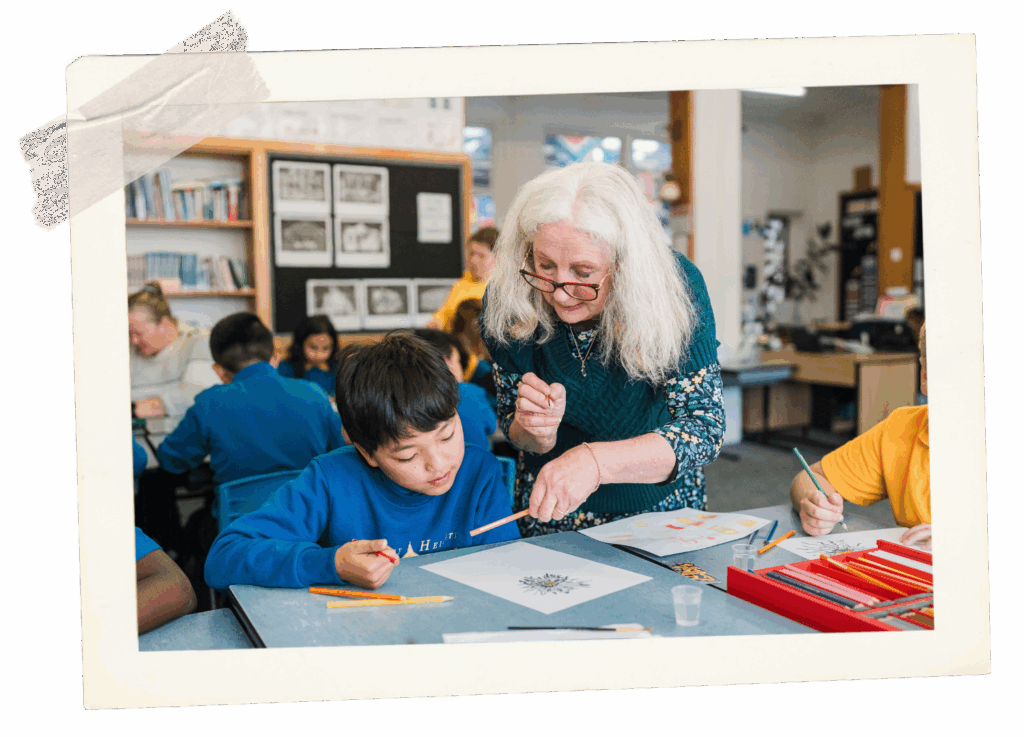 Young child with a teacher drawing. The teacher is using the non pointed end of the pencil to point at the drawing. The teacher appears to watching his colouring in.