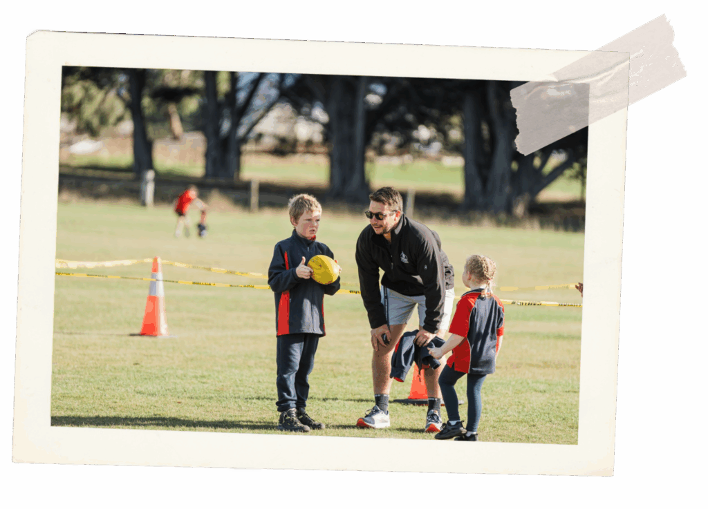 Sports teacher with two small children kicking a football.