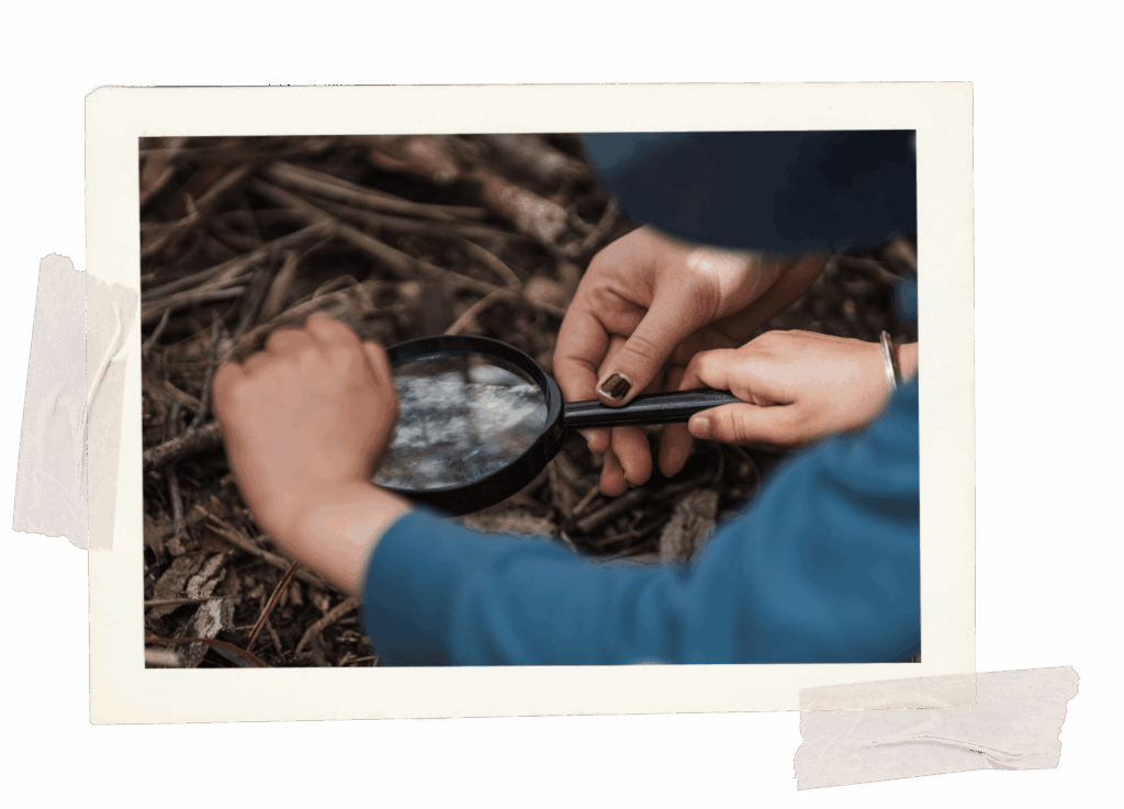 Child using a magnified glass, looking into some dirt.